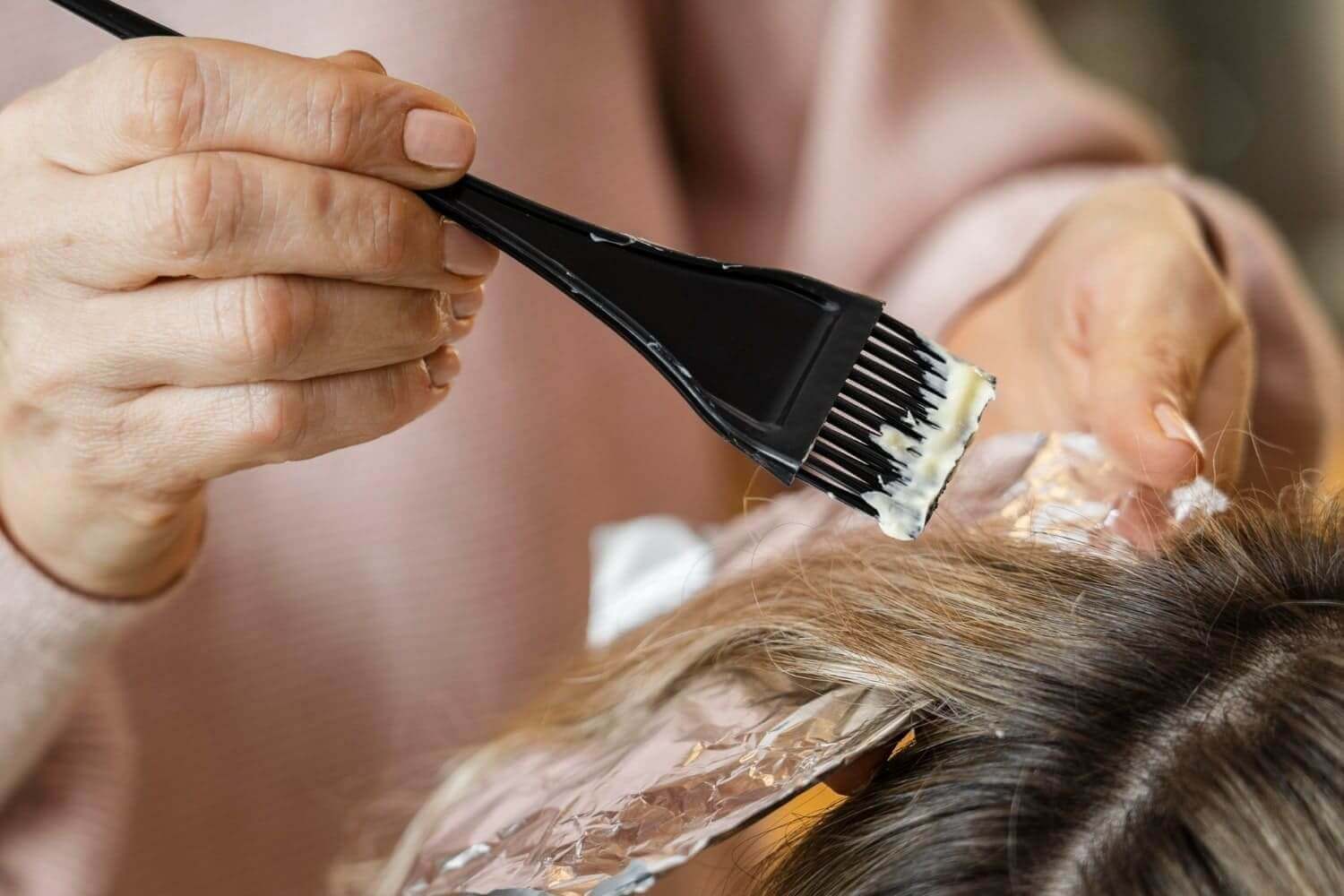 Close-up of a hand applying hair dye with a brush and foil in a salon