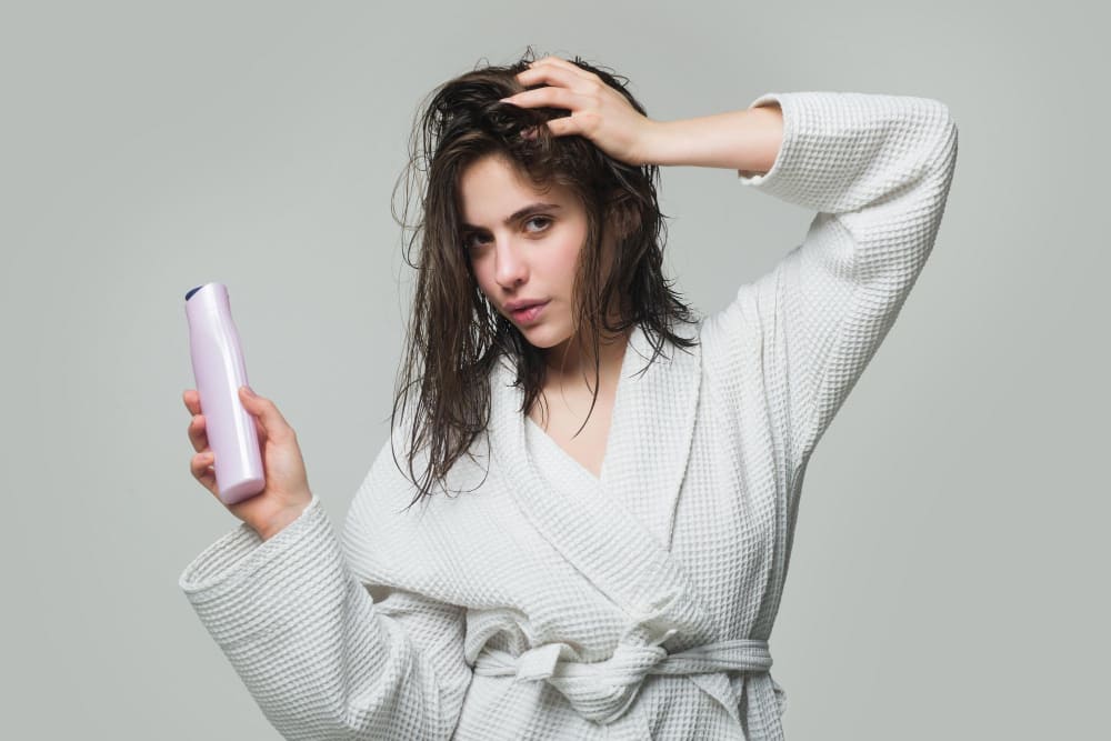 Woman in a white robe holding a shampoo bottle, with wet hair