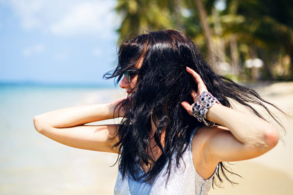 Woman with long dark hair wearing sunglasses on the beach