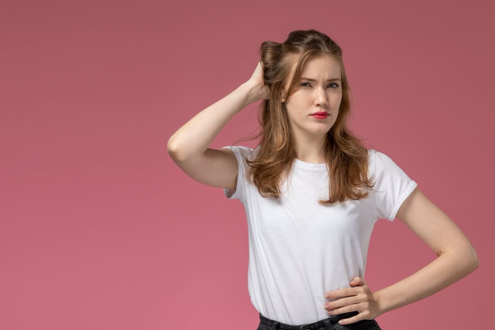Girl touching her head in front of a pink background, looking confused