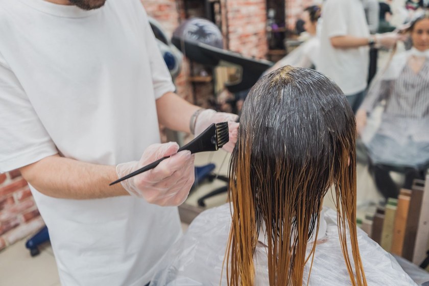 Colorist painting lightener onto sectioned hair with a tint brush during a balayage service