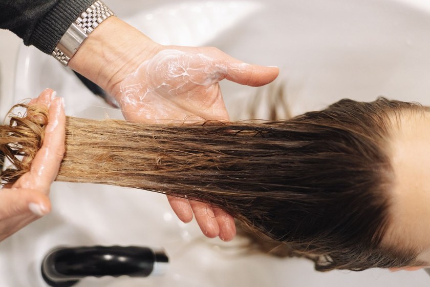 Stylist working a conditioning treatment through a client’s long wet hair at the salon backwash bowl