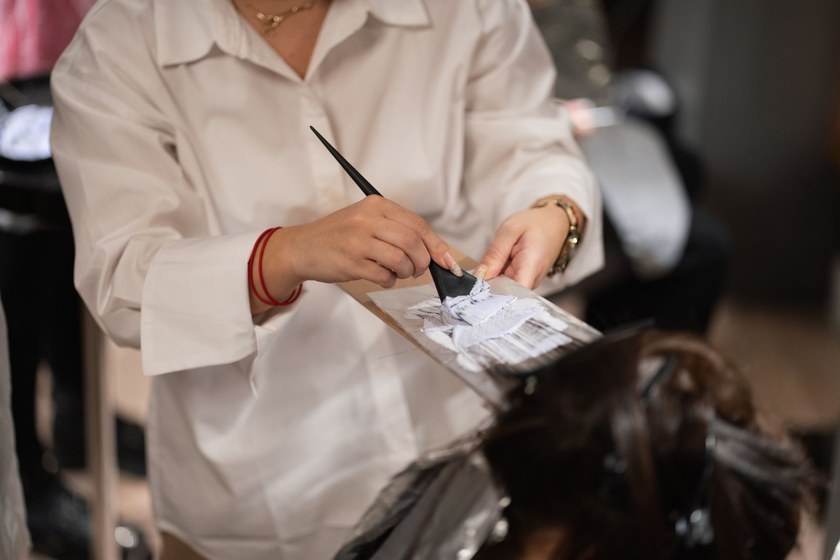 Colorist holding a tint brush and a foil packet against a sectioned head during a highlights service