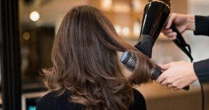 A stylist smoothing voluminous brown hair with a round brush and professional dryer