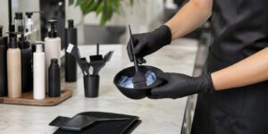 A stylist in gloves mixing hair color in a tint bowl at the salon color bar