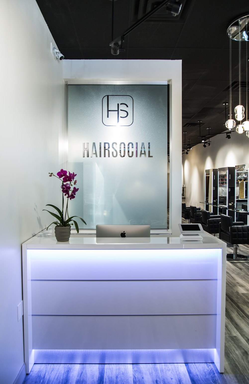 The lit white front desk at HairSocial Falls Church with the frosted HairSocial logo panel behind it