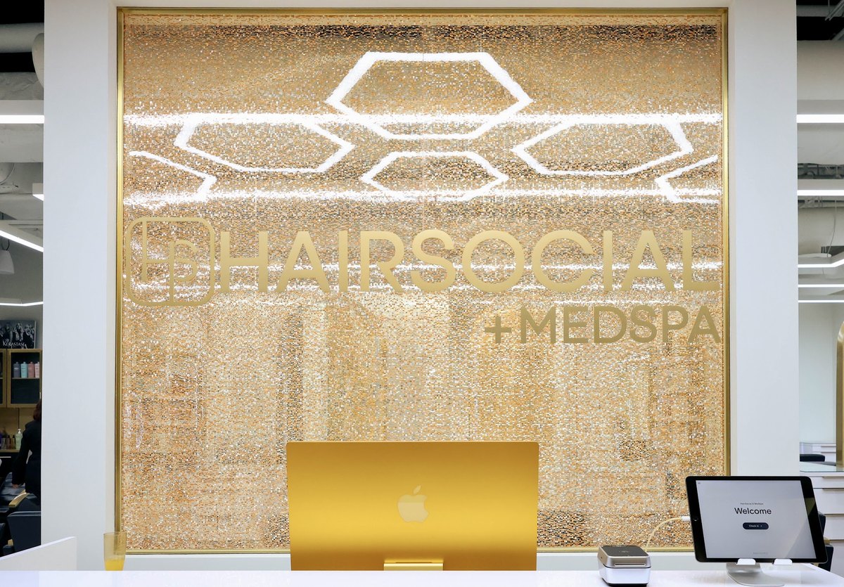 The front desk at HairSocial Tysons, with the backlit gold hexagon wall behind it