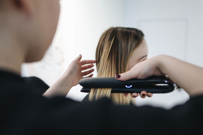 Stylist sealing a section of long hair with a flat iron during a smoothing treatment