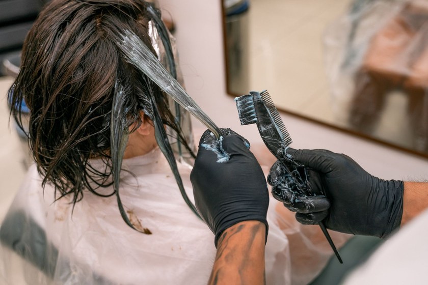 Gloved colorist applying single process color from a tint bowl to a client’s hair