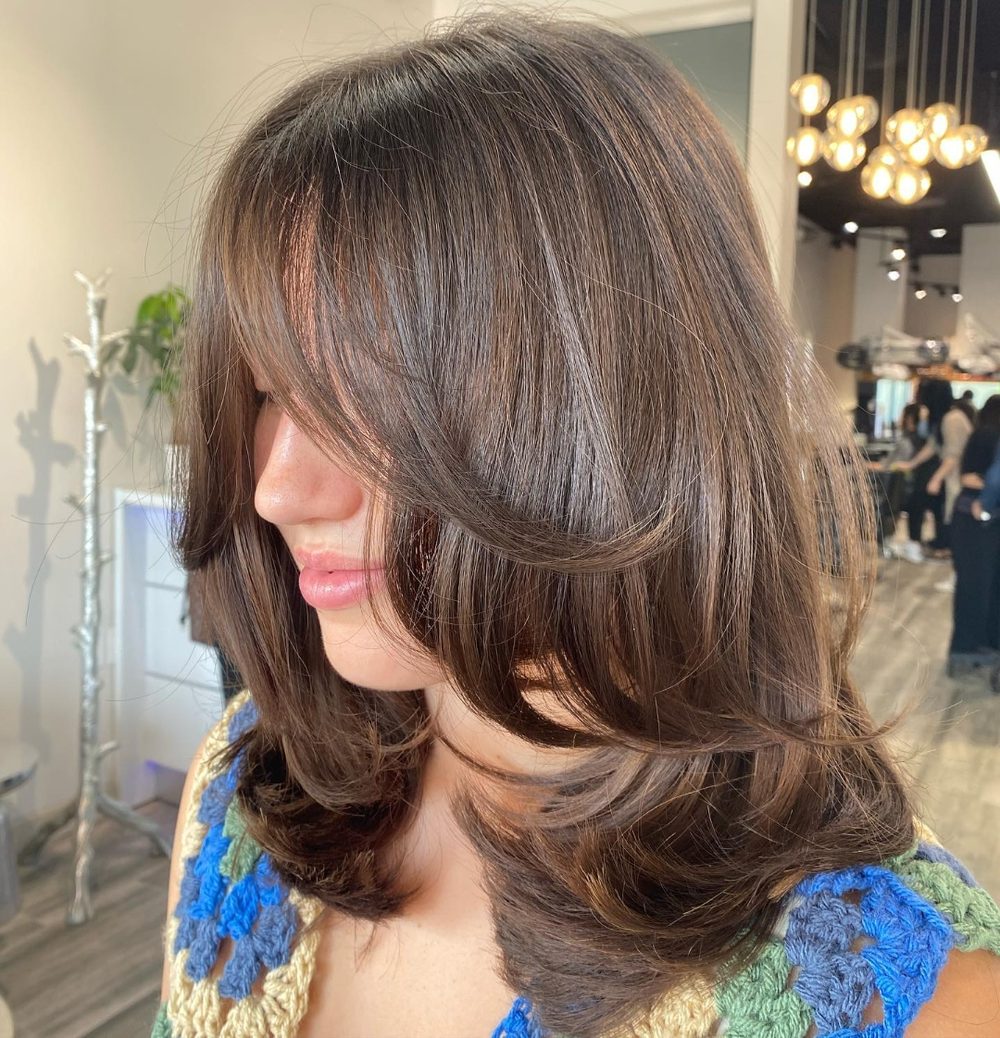 Women’s haircut in Tysons: mid-length brunette hair with face-framing layers, blow-dried with the ends turned under